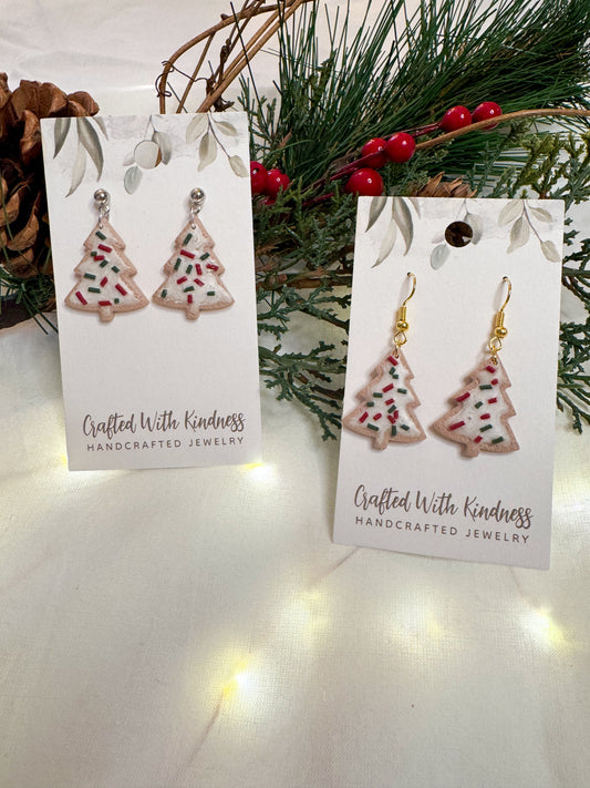 Christmas cookie earrings in the shape of Christmas trees with white frosting and green and red sprinkles.