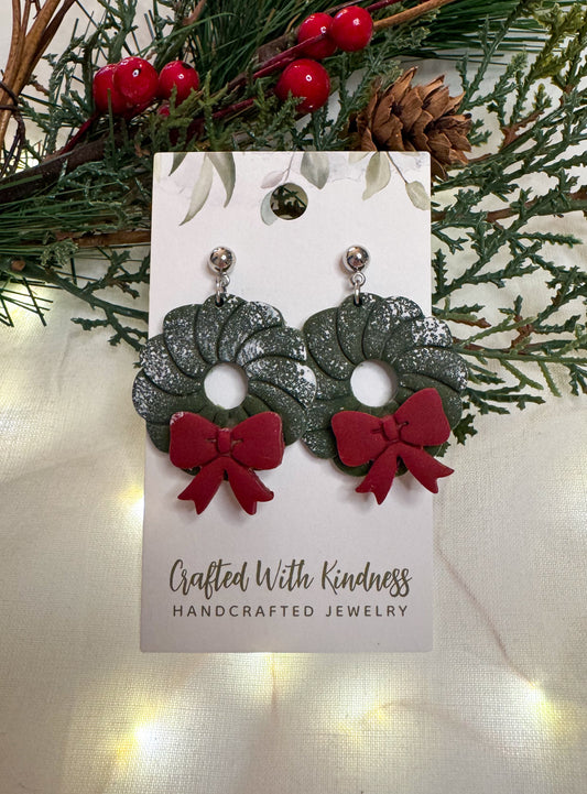 Christmas wreath earring made from polymer clay. A green wreath with a red bow and a dusting of snow on top.